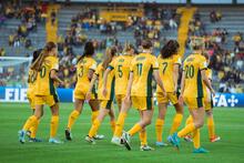 A group of Australian players with their backs to the camera, walking on the pitch in their gold Australian uniforms